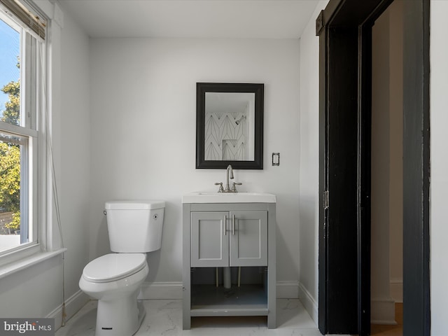 half bathroom featuring baseboards, toilet, marble finish floor, and vanity