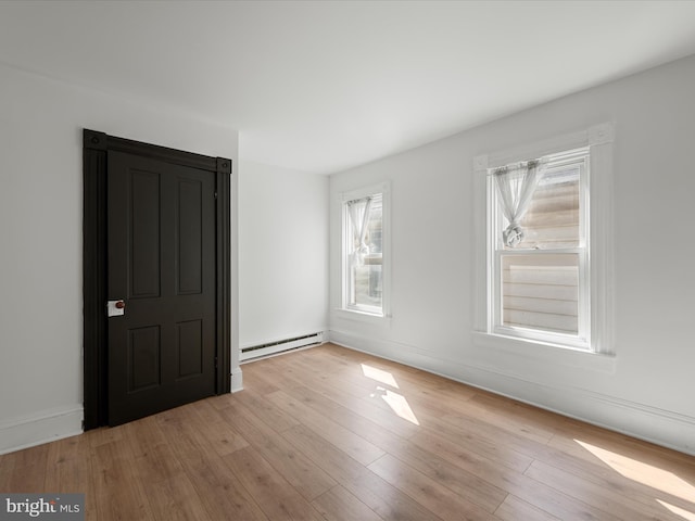 empty room with wood finished floors, baseboards, and a baseboard radiator