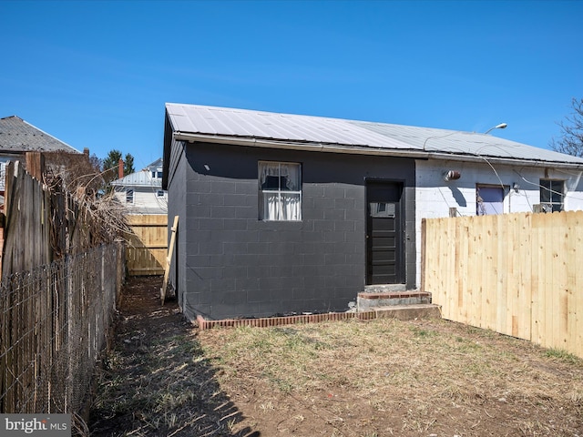 rear view of property featuring concrete block siding, a fenced backyard, and metal roof