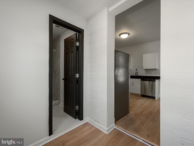 corridor with baseboards, light wood-style floors, and brick wall