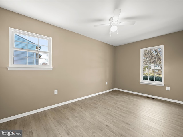 unfurnished room with a ceiling fan, visible vents, wood finished floors, and baseboards