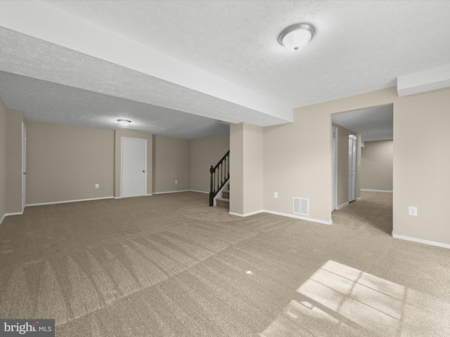 finished below grade area featuring visible vents, a textured ceiling, stairway, carpet, and baseboards