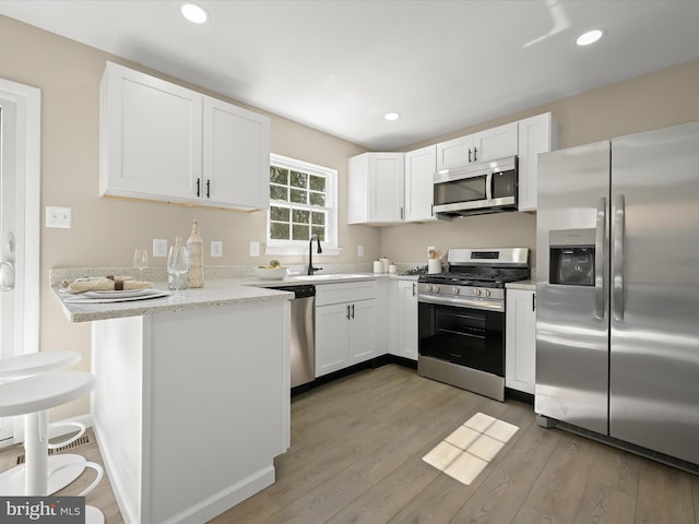 kitchen with appliances with stainless steel finishes, white cabinetry, light wood-type flooring, and a sink