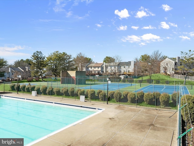 view of swimming pool featuring a tennis court, fence, and a residential view