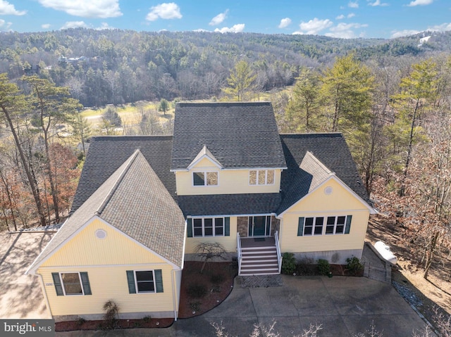 traditional-style house featuring roof with shingles and a view of trees