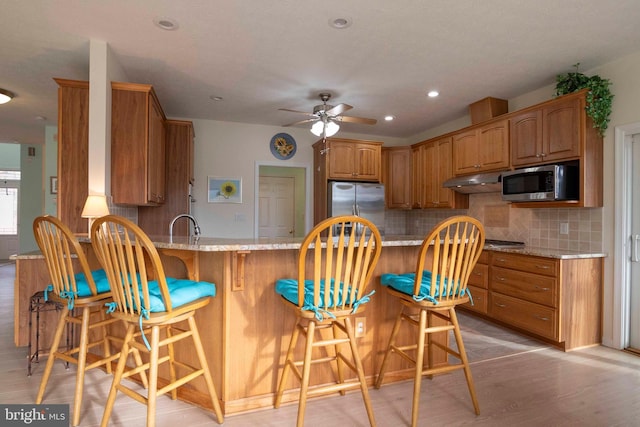 kitchen with a peninsula, appliances with stainless steel finishes, light stone counters, and decorative backsplash