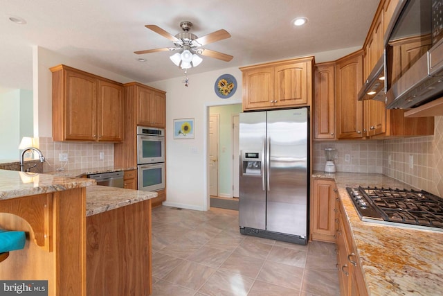 kitchen featuring brown cabinets, decorative backsplash, appliances with stainless steel finishes, a sink, and light stone countertops