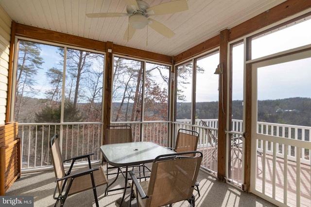 sunroom / solarium featuring wood ceiling, a ceiling fan, and a wooded view