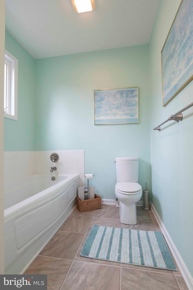 full bath with tile patterned floors, a garden tub, toilet, and baseboards