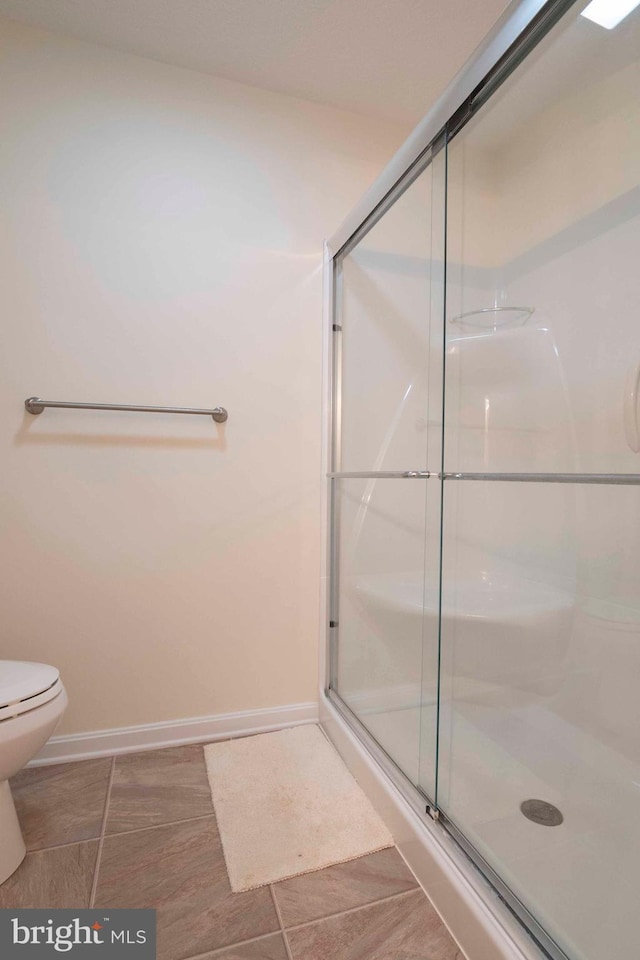 bathroom with a stall shower, toilet, and baseboards