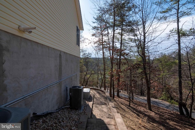 view of property exterior featuring central air condition unit and a view of trees