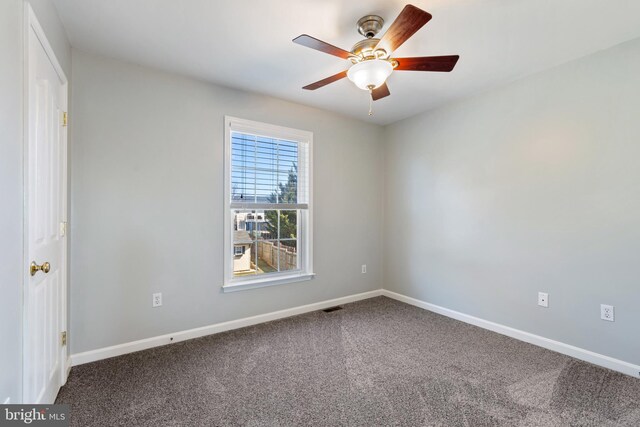 empty room with visible vents, dark carpet, a ceiling fan, and baseboards