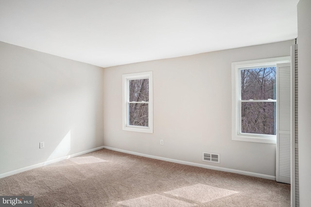 empty room featuring carpet, a healthy amount of sunlight, and visible vents