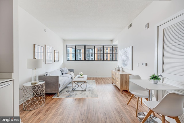 living room featuring visible vents, light wood-style flooring, a textured ceiling, and baseboards