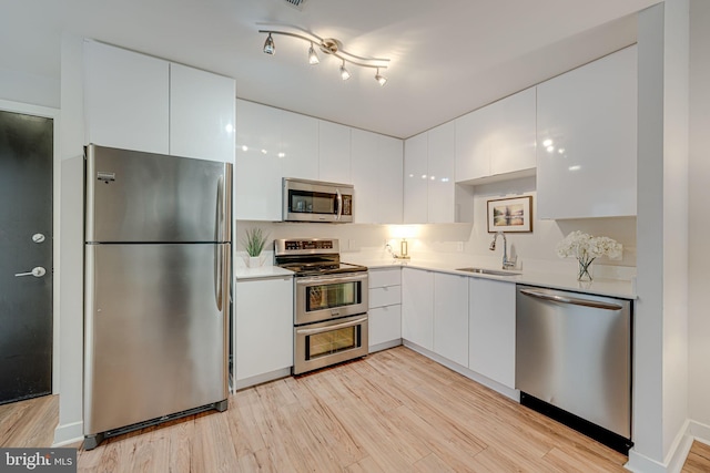 kitchen with appliances with stainless steel finishes, light wood-style floors, white cabinets, modern cabinets, and a sink