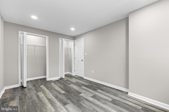 unfurnished bedroom featuring recessed lighting, wood finished floors, two closets, and baseboards