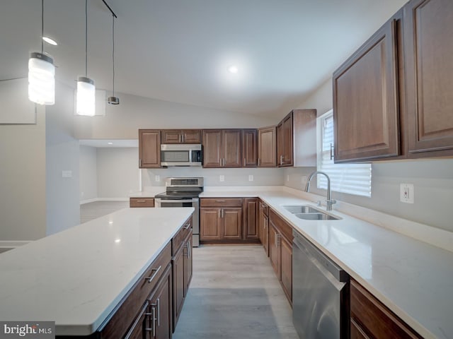 kitchen with light wood finished floors, lofted ceiling, a sink, hanging light fixtures, and stainless steel appliances