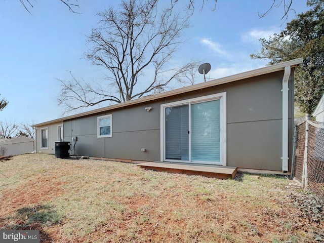 back of property featuring a yard, stucco siding, central AC, and fence