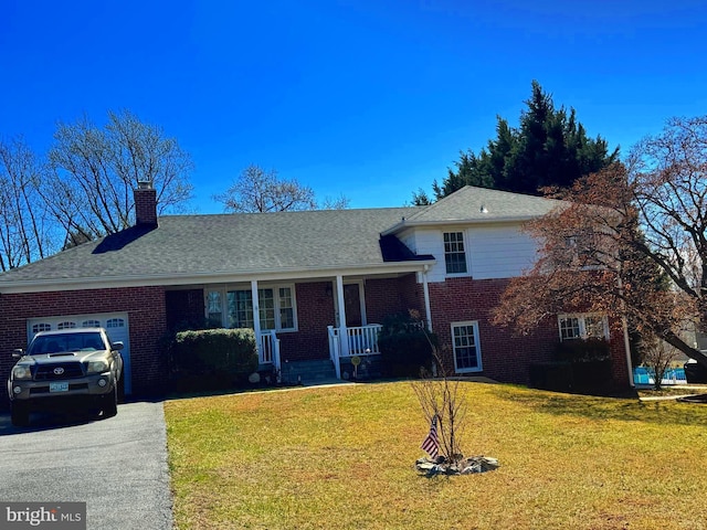 split level home featuring aphalt driveway, brick siding, a chimney, an attached garage, and a front lawn