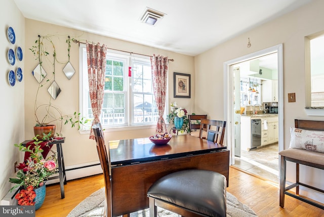 dining space featuring light wood-type flooring, visible vents, and baseboard heating