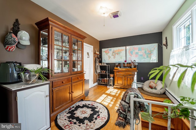 interior space with brown cabinets, a baseboard radiator, visible vents, light wood-style flooring, and glass insert cabinets