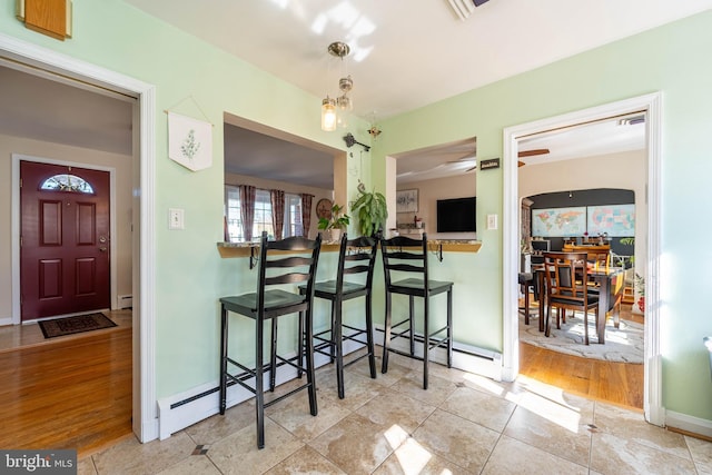 interior space featuring visible vents, baseboards, a baseboard radiator, a breakfast bar, and wood finished floors