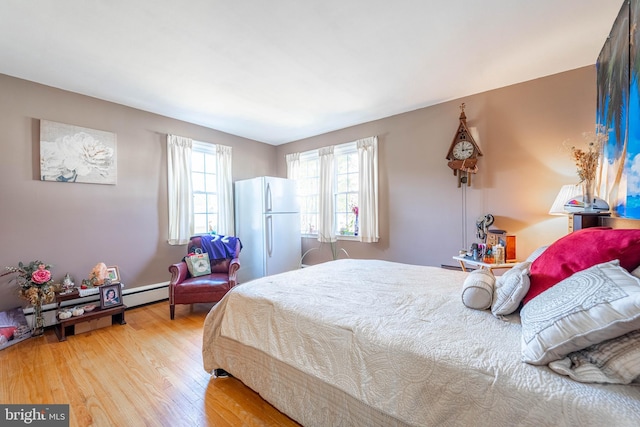 bedroom featuring a baseboard heating unit, wood finished floors, and freestanding refrigerator