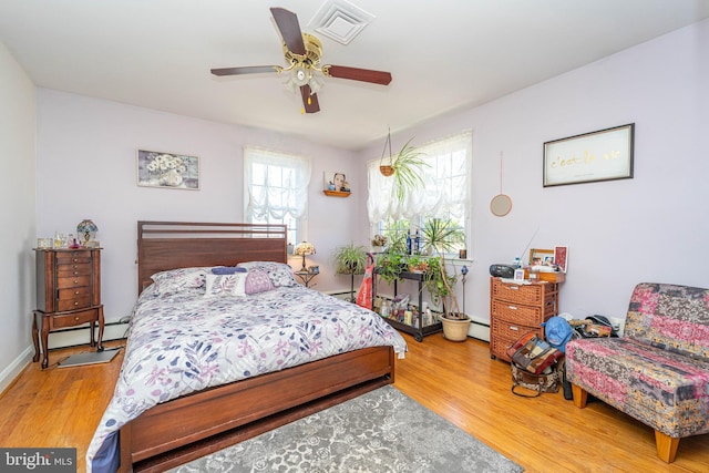 bedroom with a baseboard radiator, visible vents, and wood finished floors