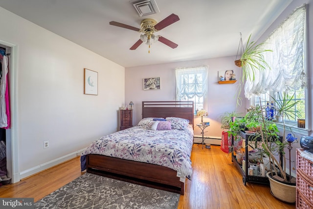 bedroom with wood finished floors, a ceiling fan, visible vents, baseboards, and baseboard heating