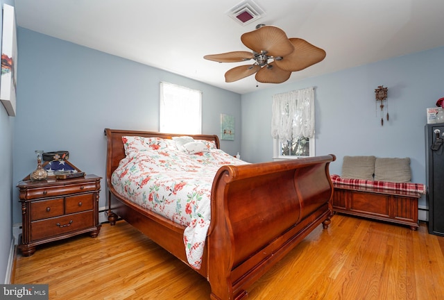 bedroom featuring a baseboard heating unit, light wood-style flooring, visible vents, and a ceiling fan