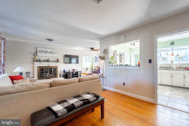 living area with light wood-style floors, baseboards, a ceiling fan, and a glass covered fireplace