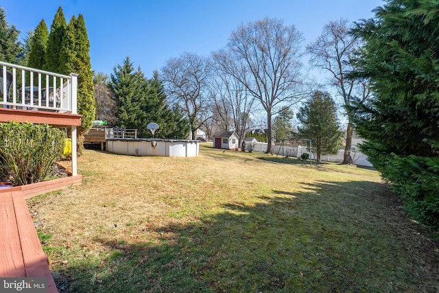 view of yard with an outdoor pool, fence, a deck, an outdoor structure, and a shed