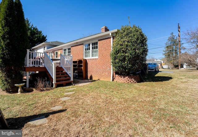 view of front of property with a deck, brick siding, a chimney, and a front lawn