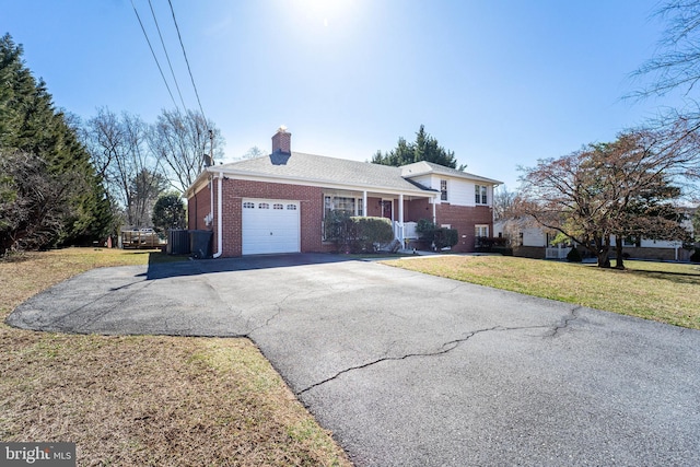 view of front facade featuring a garage, brick siding, a chimney, aphalt driveway, and a front yard