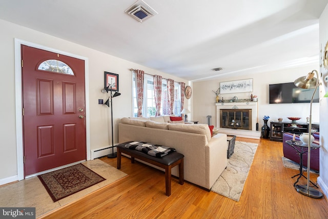 living room featuring a baseboard heating unit, wood finished floors, a glass covered fireplace, and visible vents