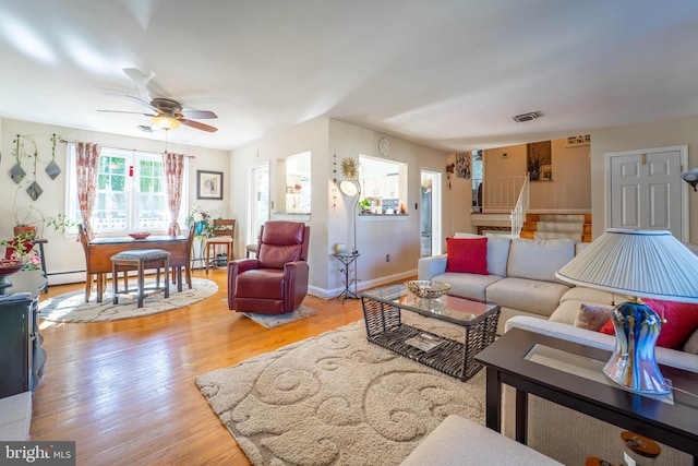 living area with a baseboard radiator, visible vents, stairway, ceiling fan, and wood finished floors