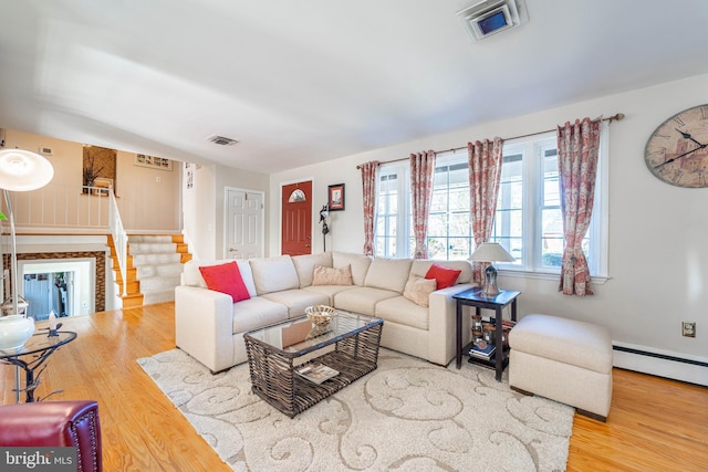 living room with stairs, a baseboard heating unit, wood finished floors, and visible vents