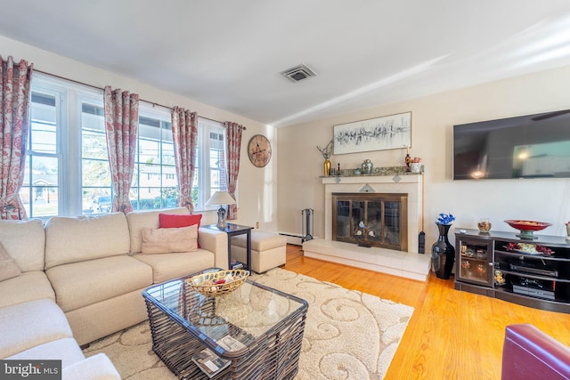 living room with a baseboard radiator, a tile fireplace, visible vents, and wood finished floors