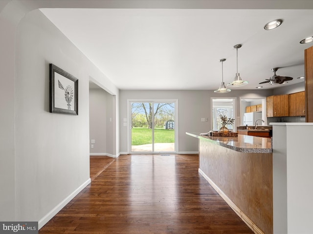 kitchen with ceiling fan, dark wood finished floors, brown cabinetry, a sink, and baseboards