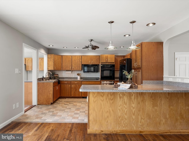 kitchen with a ceiling fan, backsplash, brown cabinetry, pendant lighting, and black appliances
