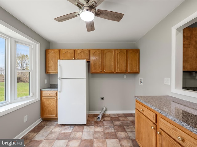 kitchen with brown cabinetry, freestanding refrigerator, baseboards, and a ceiling fan
