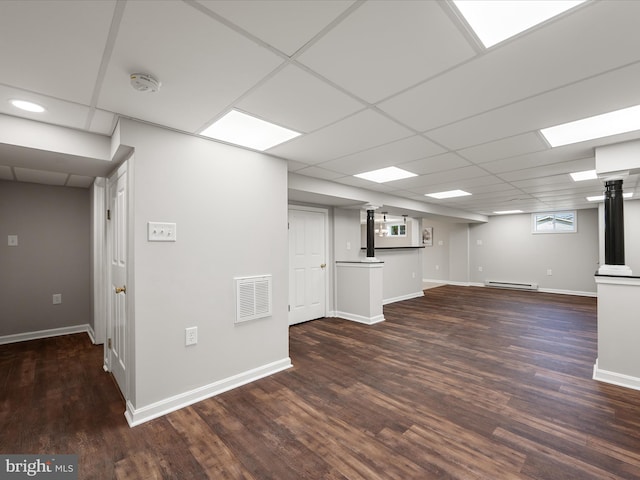 basement with a paneled ceiling, visible vents, wood finished floors, a baseboard radiator, and baseboards