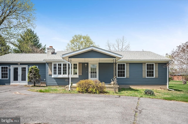 ranch-style home with a porch, roof with shingles, french doors, and a chimney