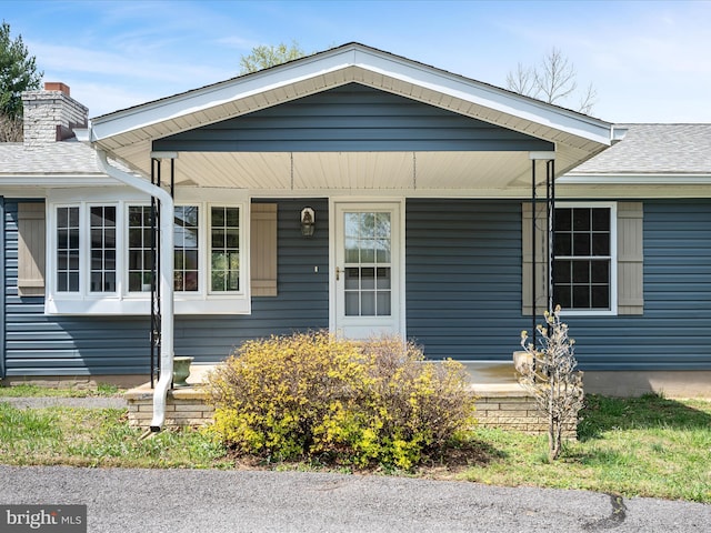 view of front of home with roof with shingles, a chimney, and covered porch