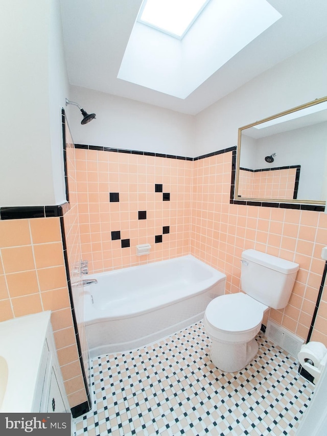 full bathroom with a skylight, tile walls, shower / bathtub combination, toilet, and tile patterned floors