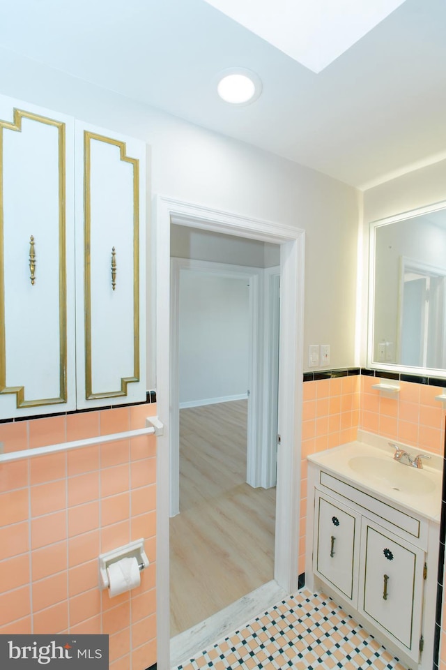 bathroom featuring tile patterned flooring, recessed lighting, vanity, tile walls, and wainscoting