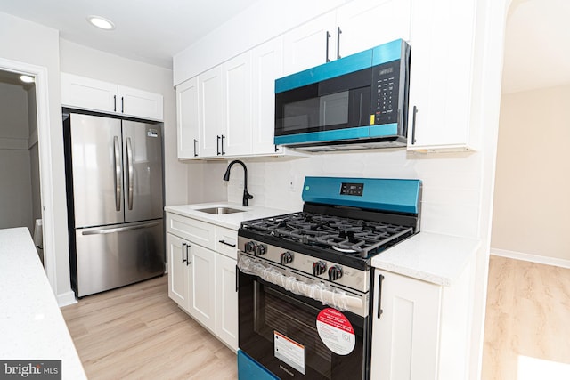 kitchen with stainless steel appliances, white cabinetry, a sink, and light wood-style flooring