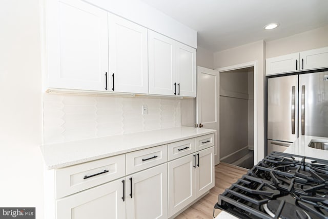 kitchen featuring light wood-type flooring, freestanding refrigerator, white cabinets, and light stone countertops