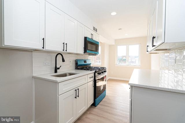 kitchen featuring stainless steel gas range, a sink, light wood-style flooring, and white cabinets