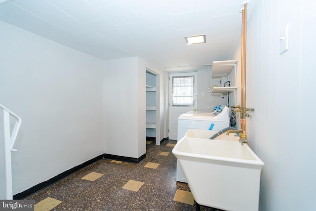 laundry room with dark floors, washer and clothes dryer, a sink, laundry area, and baseboards